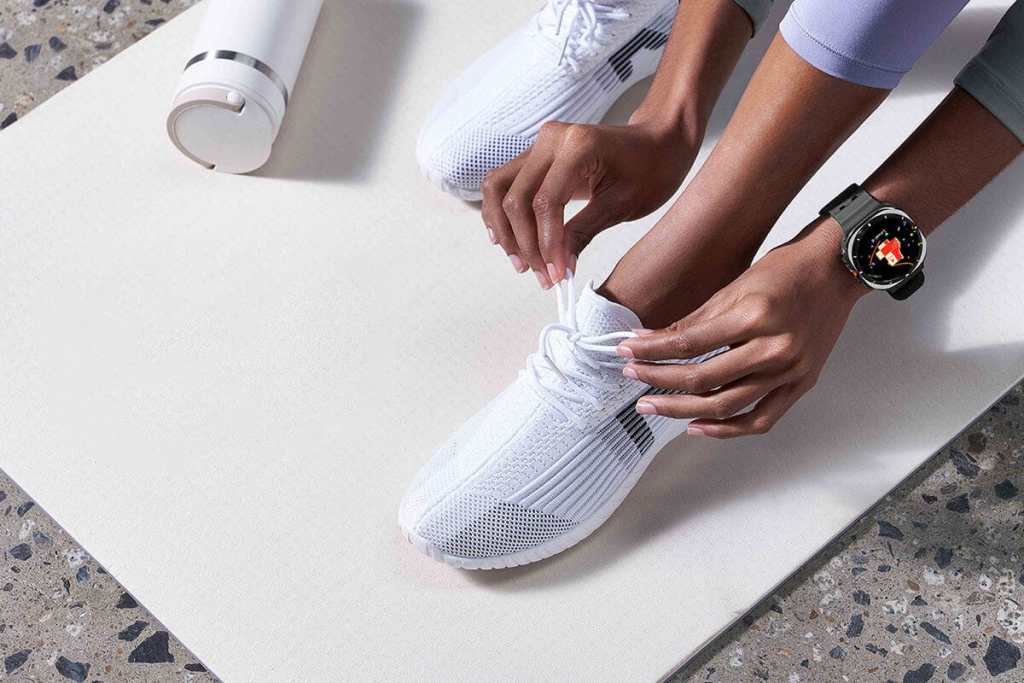 Close-up of a person tying their shoelaces while wearing a Galaxy Watch on their wrist, with a water bottle in the background.