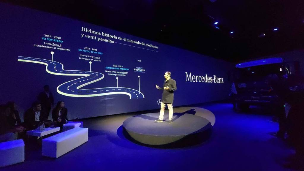 Presentación de los nuevos camiones Atego y Accelo de Mercedes-Benz, destacando su evolución en el mercado peruano, con un orador en un escenario y visuales sobre un fondo oscuro.