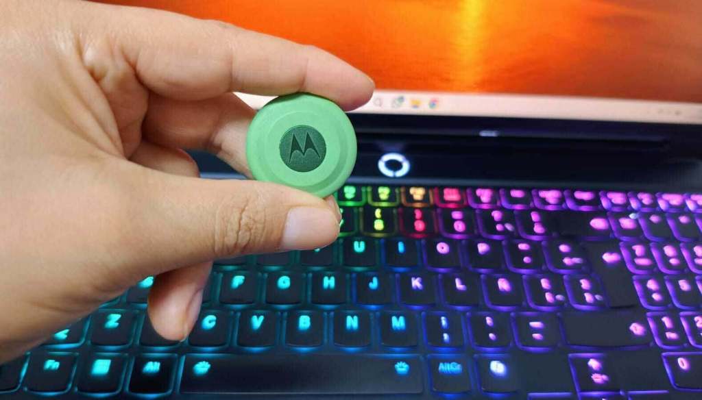 Una mano sostiene un objeto verde con el logo de Motorola, frente a un teclado iluminado con luces de colores.