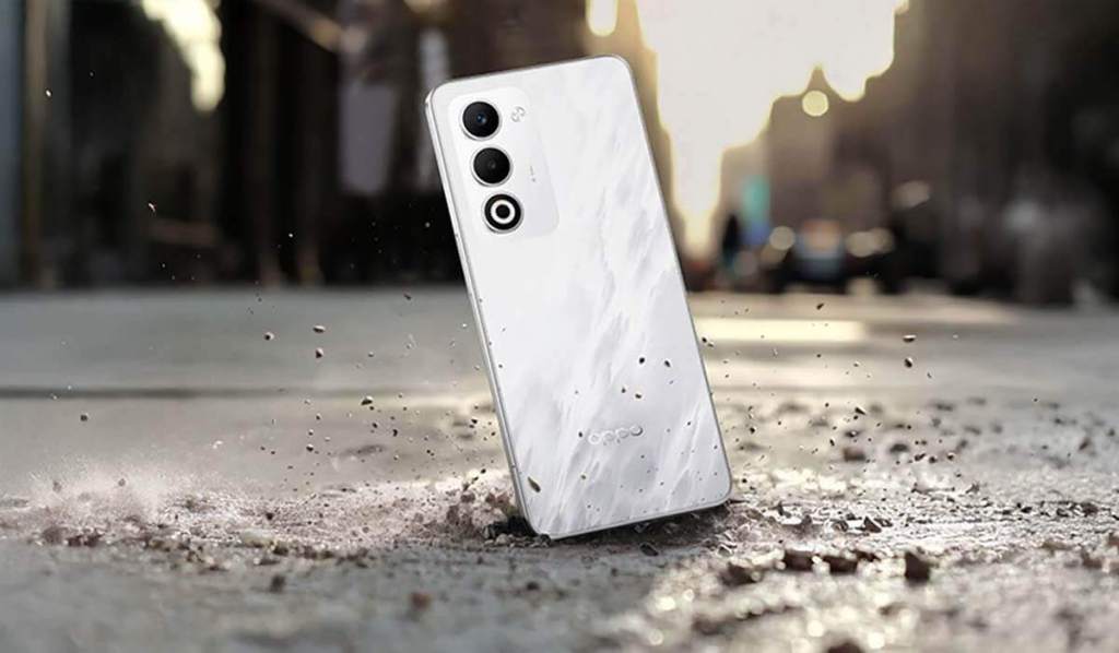 Un teléfono inteligente OPPO A5 5G en el suelo, con un diseño elegante de color blanco, mostrando su resistencia al impacto y la tecnología avanzada.