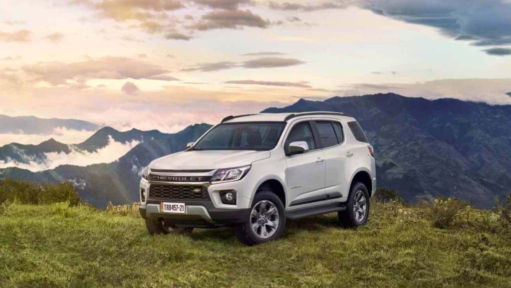 Vehículo Chevrolet SUV blanco estacionado sobre un fondo montañoso y nublado al atardecer.