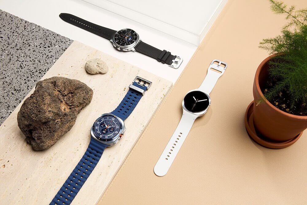Dos relojes inteligentes Galaxy Watch8 sobre una superficie de piedra y una mesa de color claro, acompañados de una roca y una planta en maceta.