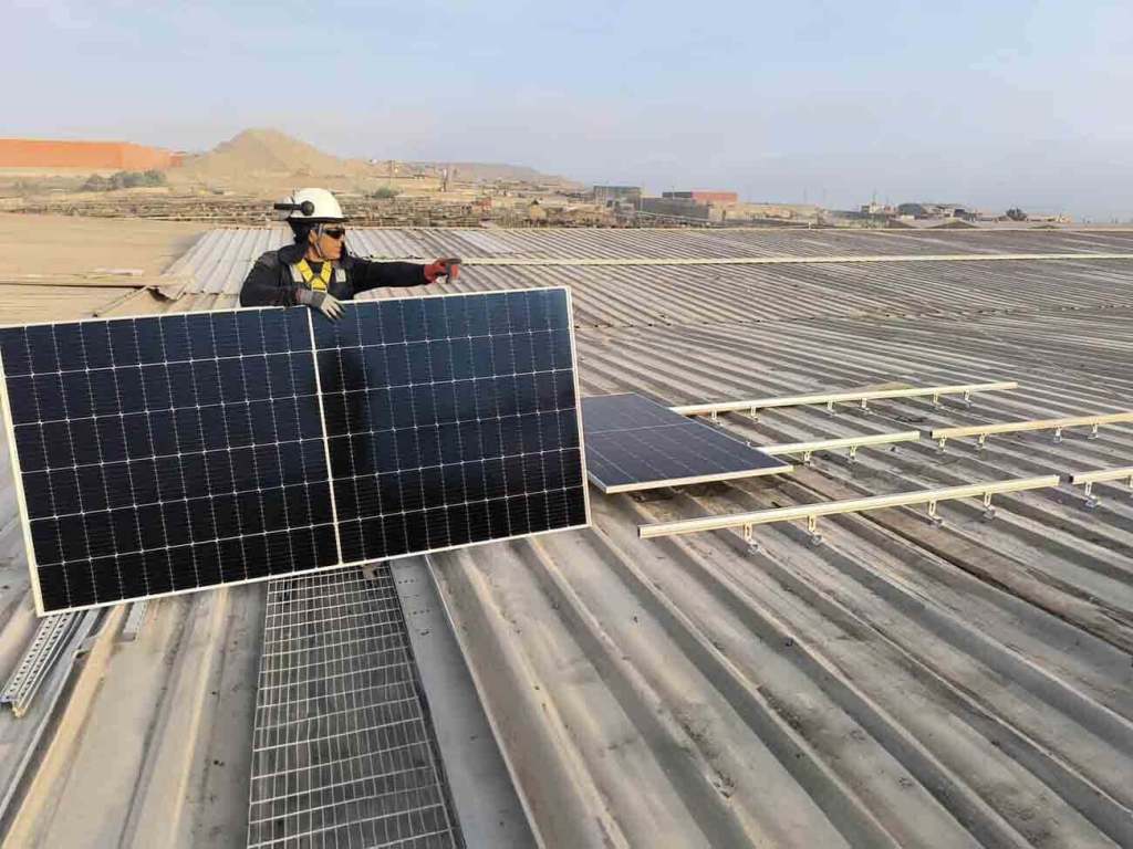 Un técnico sostiene paneles solares en el techo de una granja avícola en Perú, mientras se trabaja en la instalación de un sistema de energía solar híbrido.