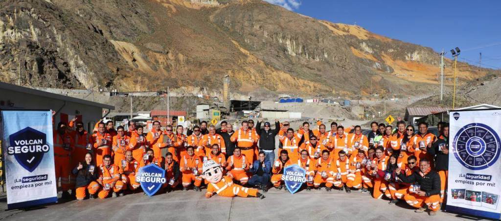 Grupo de trabajadores de Volcan Compañía Minera en un evento de lanzamiento de 'Volcan Seguro', todos vistiendo uniformes de seguridad naranja, posando junto a un banner que promueve la seguridad laboral en un entorno minero.