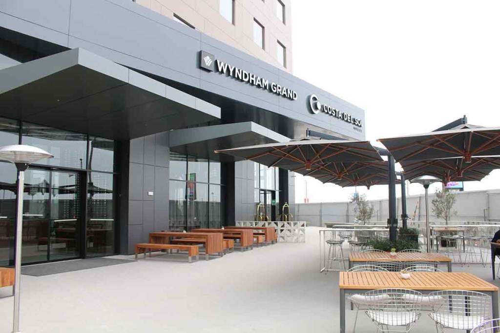 Fachada del Wyndham Grand Costa del Sol Lima Airport, el primer hotel cinco estrellas del nuevo terminal del Aeropuerto Internacional Jorge Chávez, con mesas al aire libre y áreas de descanso.