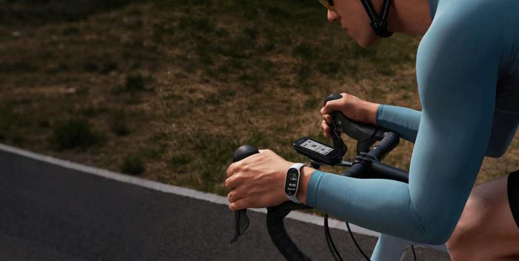 Una persona montando en bicicleta, con una camiseta de manga larga y gafas de sol, sosteniendo el manillar mientras utiliza la Xiaomi Smart Band 10 en su muñeca.