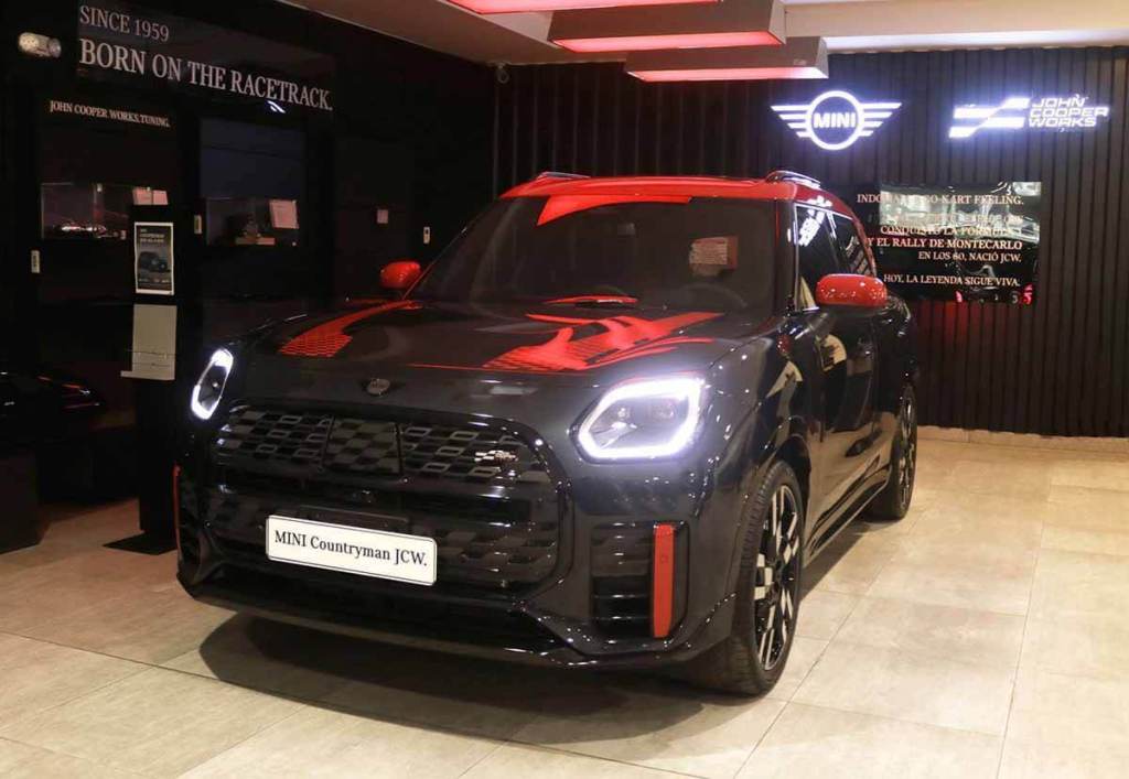 Vista frontal del MINI Countryman JCW, un SUV deportivo con detalles en rojo y negro, exhibido en un showroom de MINI.
