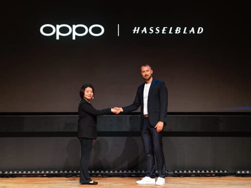 Representantes de OPPO y Hasselblad estrechándose la mano en un evento de anuncio de colaboración estratégica, con logos de ambas marcas en el fondo.