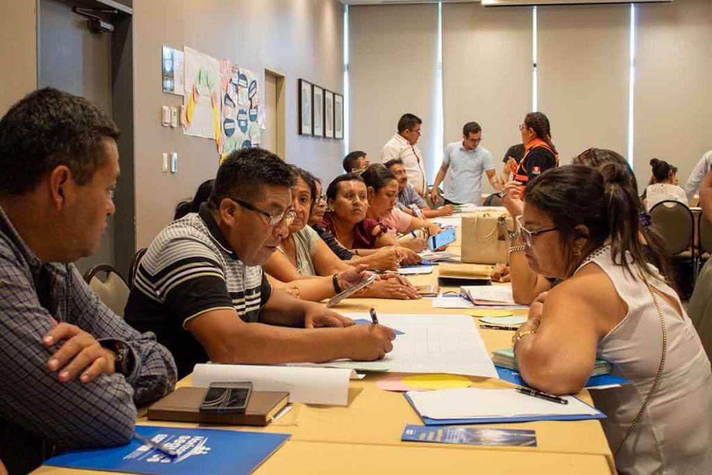Grupo de personas participando en una reunión, discutiendo sobre la gestión del riesgo de desastres en un contexto educativo.