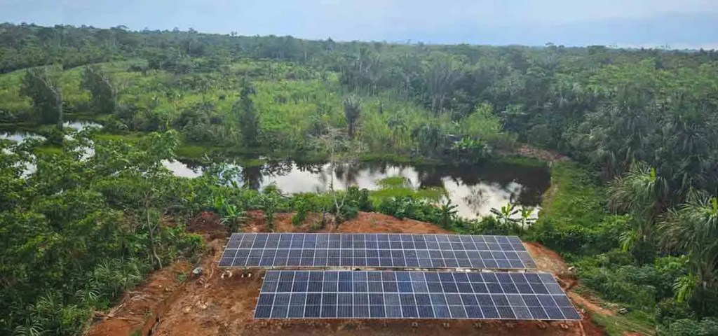 Paneles solares instalados en un área verde rural de la Amazonía peruana, junto a un cuerpo de agua, en el contexto de un proyecto de electrificación sostenible.