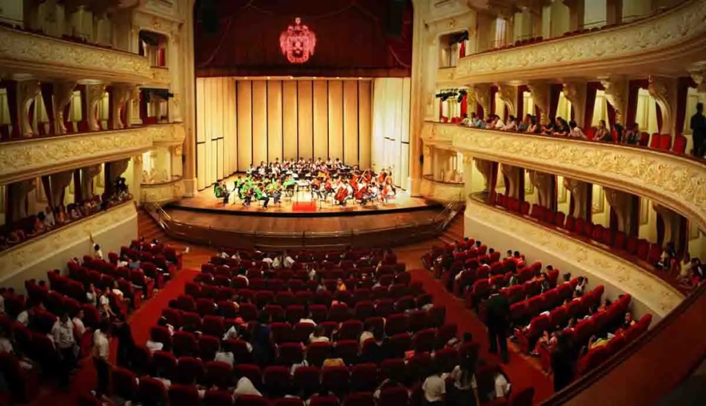 Vista del Teatro Municipal de Lima durante una representación, con una orquesta en el escenario y asientos ocupados por el público.