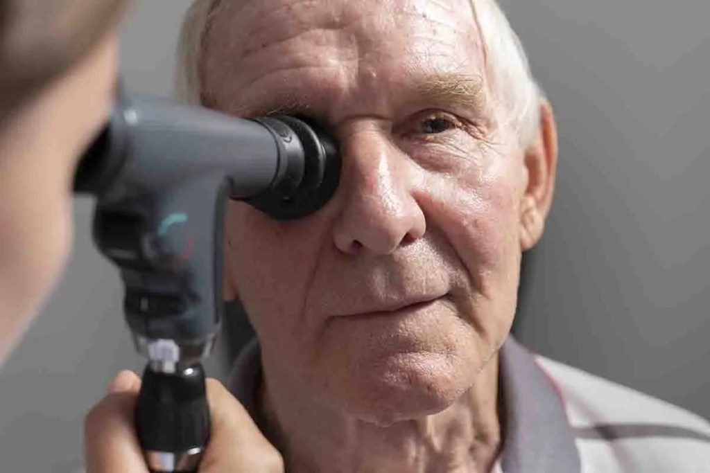 Un médico examina el ojo de un paciente mayor con un oftalmoscopio en un consultorio.