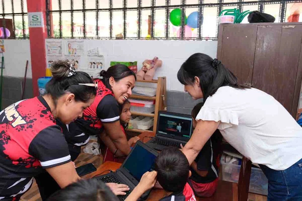 Grupo de personas en un aula, interactuando con laptops y sonriendo mientras aprenden juntos.