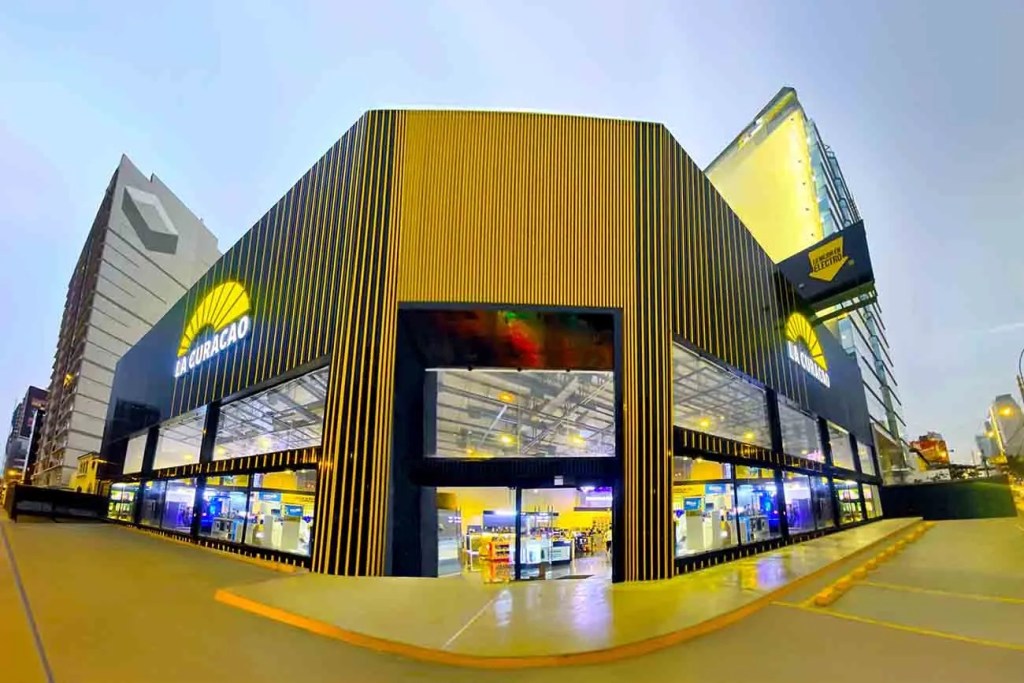 Vista exterior de la tienda renovada La Curacao en San Isidro, destacando su diseño moderno con fachada de madera y grandes ventanales iluminados.