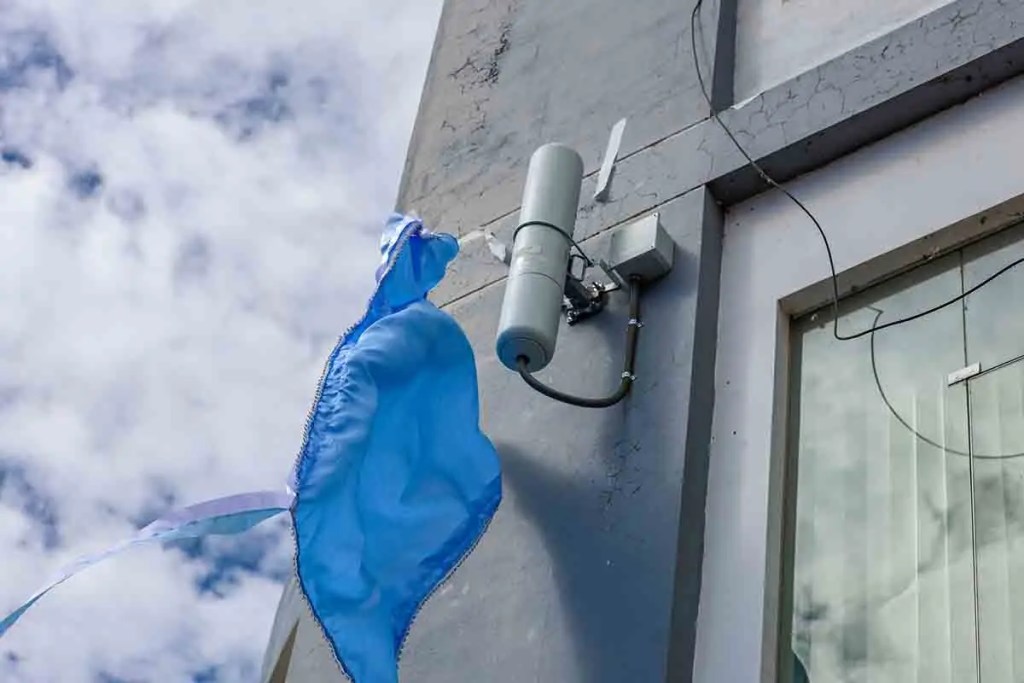 Antena de tecnología Wi-Fi 7 instalada en la pared de un edificio, con una tela azul ondeando al lado, bajo un cielo nublado.