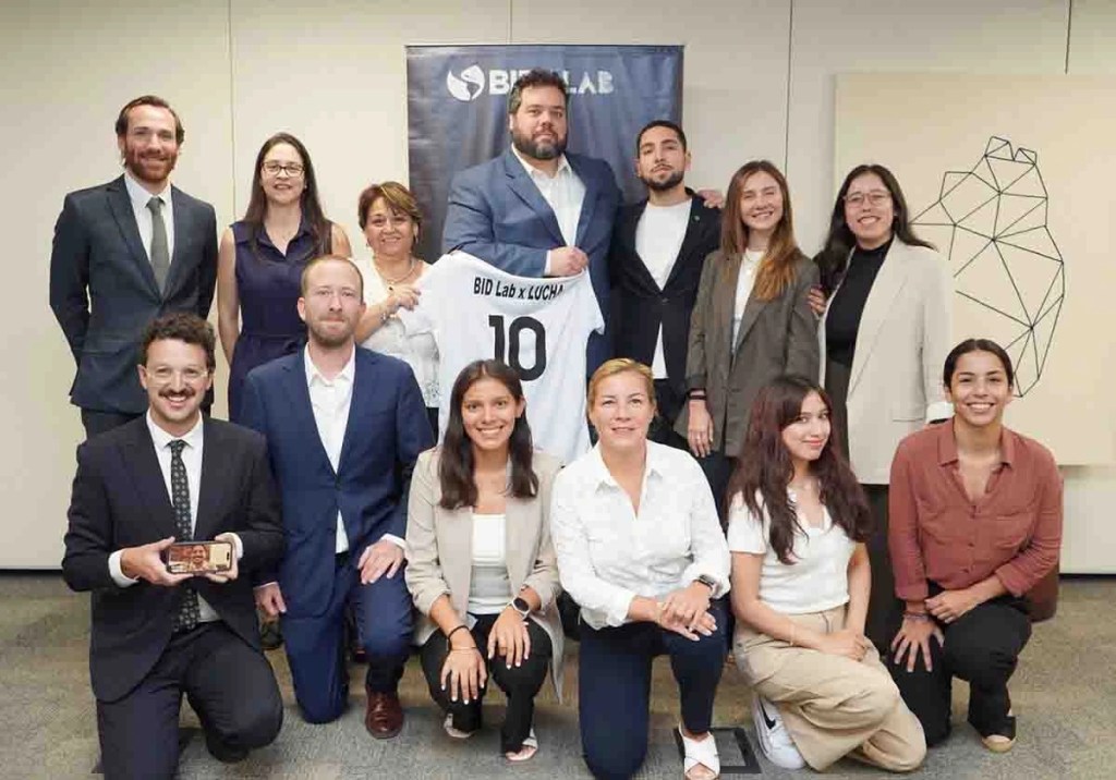 Grupo de personas posando para una foto en un evento de colaboración entre BID Lab y LUCHA, con sonrisas y una camiseta que dice 'BID Lab x LUCHA' en el centro.