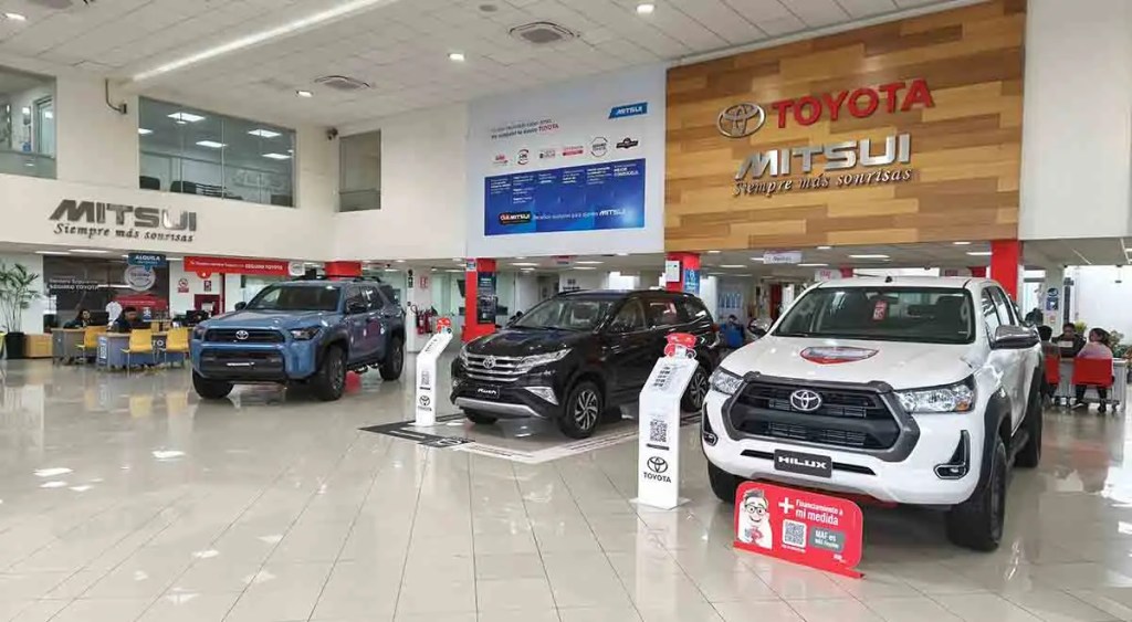 Interior de concesionaria Mitsui Automotriz con varios vehículos Toyota expuestos, incluyendo un SUV y camionetas Hilux, mostrando el logotipo de Toyota y el lema 'Siempre más sonrisas'.