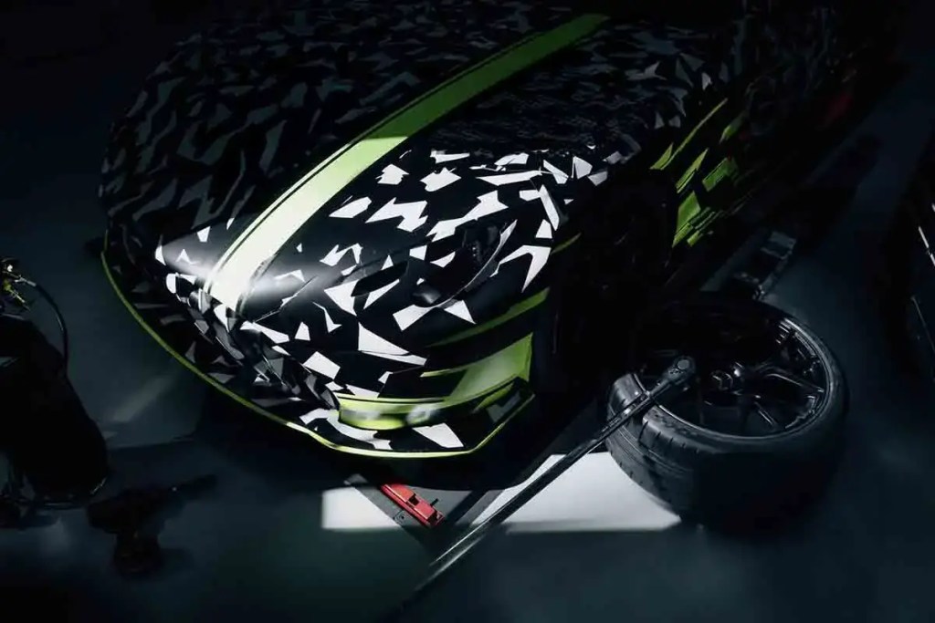 Vista cercana del nuevo concepto de auto deportivo Mercedes-AMG GT TRACK SPORT con un diseño camuflado y detalles en verde neón, en un entorno de taller.