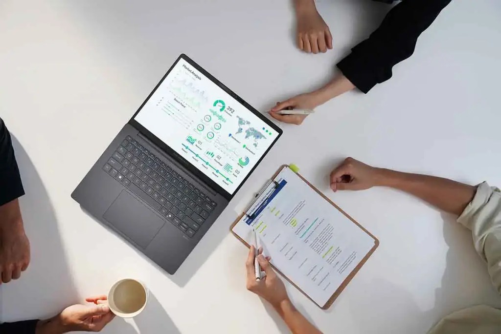 Un grupo de personas analizando datos en una computadora portátil, con gráficos y métricas en la pantalla, y papeles con notas en una mesa.