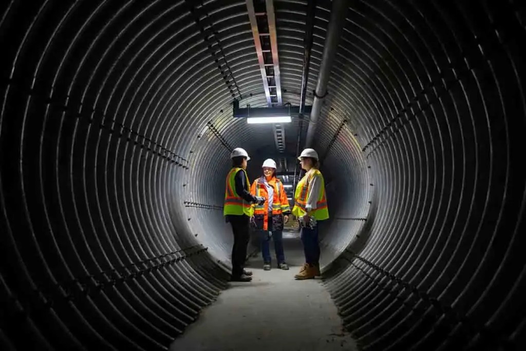 Tres profesionales conversando en un túnel de construcción, vistiendo cascos y chalecos reflectantes.