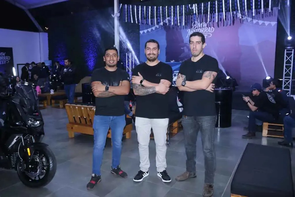 Tres hombres posando en un evento de BMW Motorrad en Perú, junto a una motocicleta y decoraciones del festival.