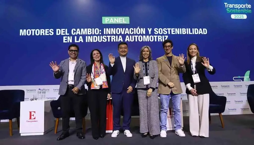 Panel de discusión en el evento Transporte Sostenible 2025, con participantes levantando la mano y sonriendo frente a un fondo que incluye el título del panel sobre innovación y sostenibilidad en la industria automotriz.