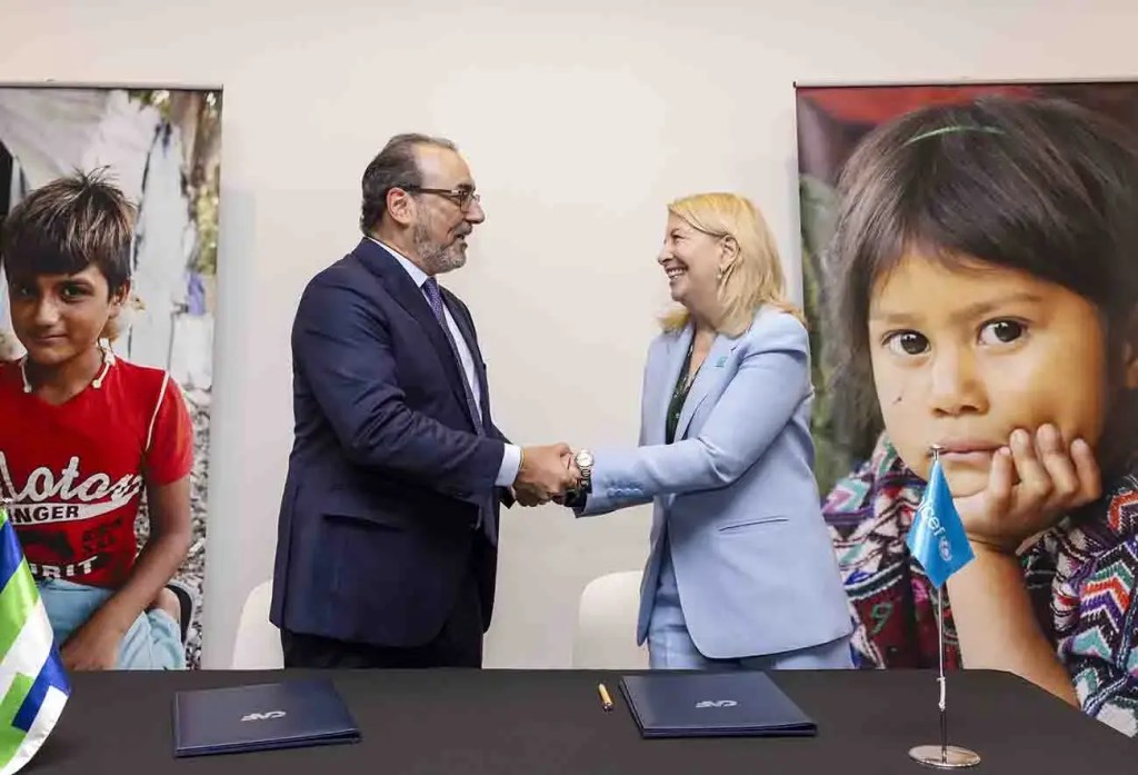 Funcionarios de CAF y UNICEF estrechando manos durante el lanzamiento de la iniciativa Banco Futuro LAC, con imágenes de niños de fondo.