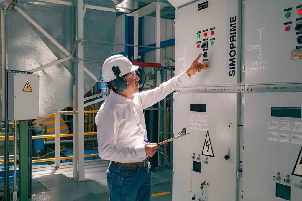 Ingeniero revisando un panel de control eléctrico en una planta de energía, usando casco y auriculares de seguridad.