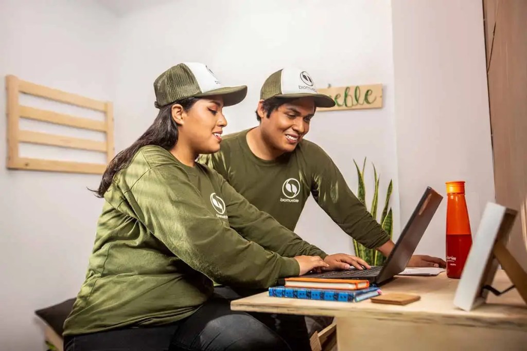 Dos jóvenes colaborando en un proyecto frente a una laptop en un ambiente de trabajo acogedor.