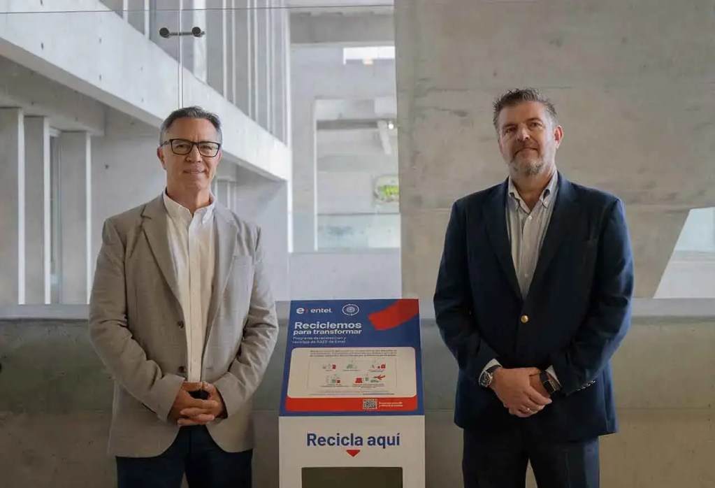 Dos hombres de pie junto a un contenedor de reciclaje de residuos electrónicos con el logo de Entel y el texto 'Reciclemos para transformar' en un entorno moderno.