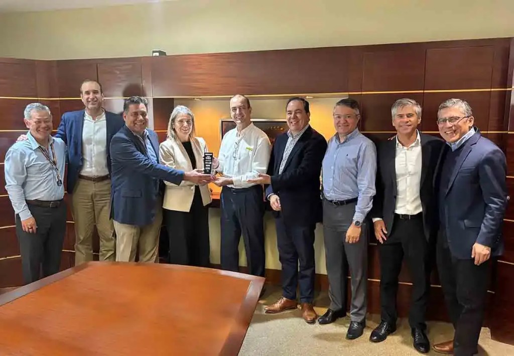 Grupo de personas en un ambiente de oficina sosteniendo un premio, con muebles de madera y decoración moderna en el fondo.