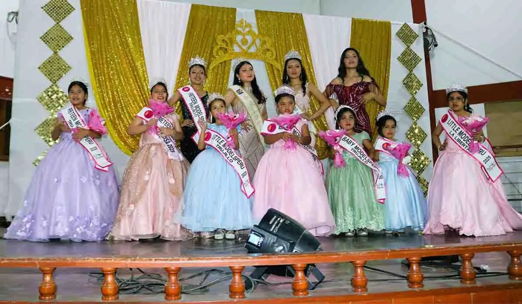 Grupo de niñas en vestidos de gala, sosteniendo flores y con coronas, en un evento de modelaje y empoderamiento femenino.