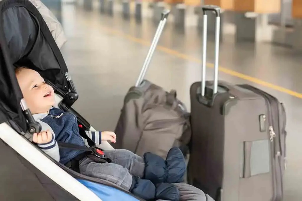Un bebé sonriendo en un cochecito junto a maletas en un aeropuerto.