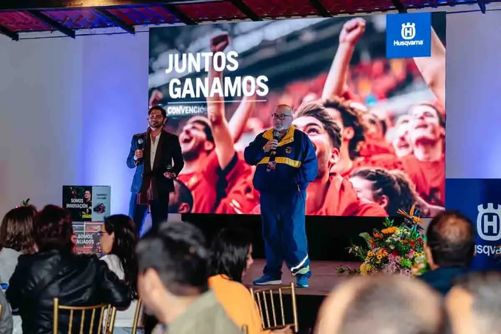 Presentadores en el escenario durante la Convención Anual de Ventas 2025 de Husqvarna en Perú, con un fondo que muestra la frase 'Juntos Ganamos' y un público atento.