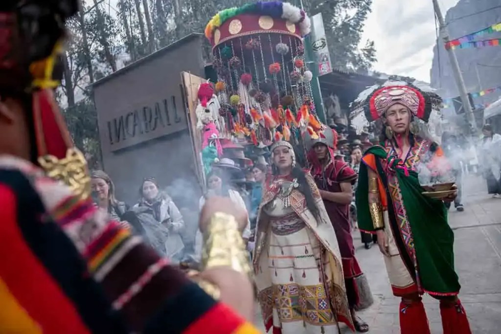 Grupo de personas en vestimentas tradicionales andinas durante un evento cultural en Cusco, con un fondo que incluye el logo de Inca Rail.