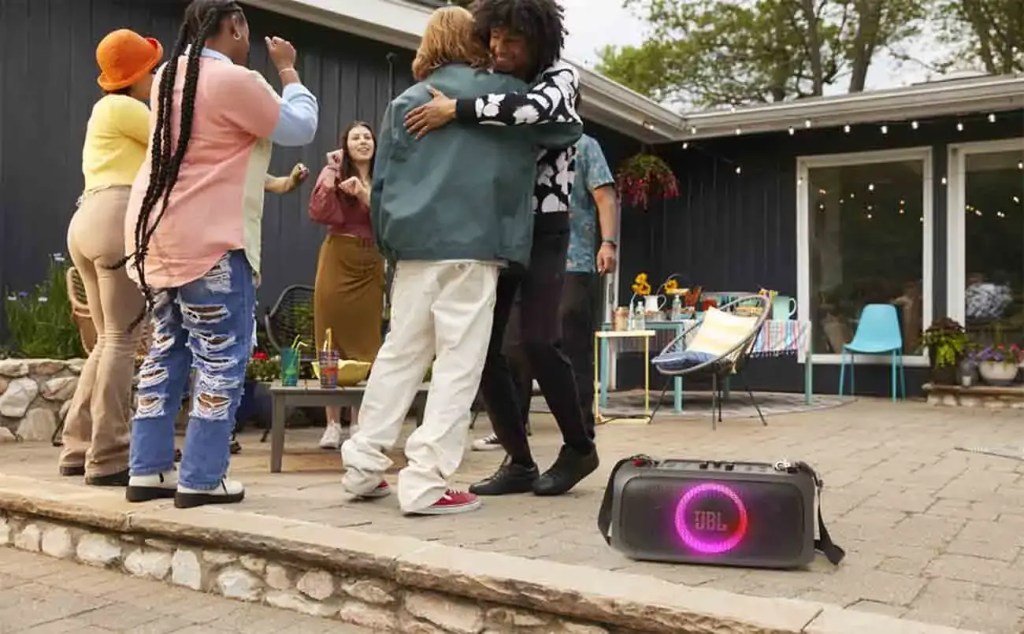 Grupo de amigos disfrutando de una fiesta al aire libre, con un altavoz JBL en primer plano, música y buena compañía.