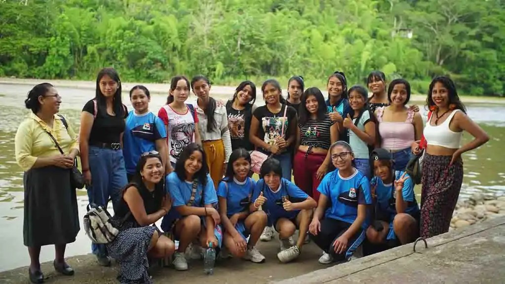 Grupo de jóvenes y adultos posando juntos al aire libre, junto a un cuerpo de agua, rodeados de vegetación exuberante.