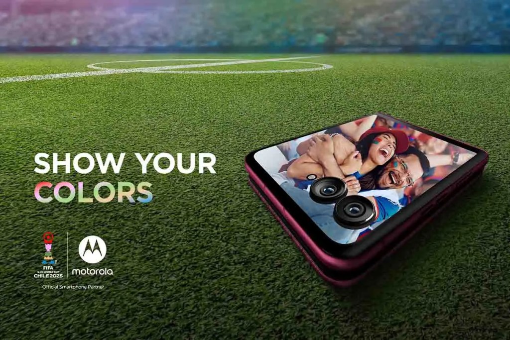 Un teléfono Motorola con una imagen de aficionados disfrutando el fútbol en un campo verde, con el texto 'SHOW YOUR COLORS' en la parte inferior.