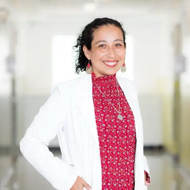 La Dra. Patricia Paredes, nueva Directora Médica de Pacífico Salud, sonríe mientras viste una bata blanca y una blusa roja con flores en un entorno clínico.