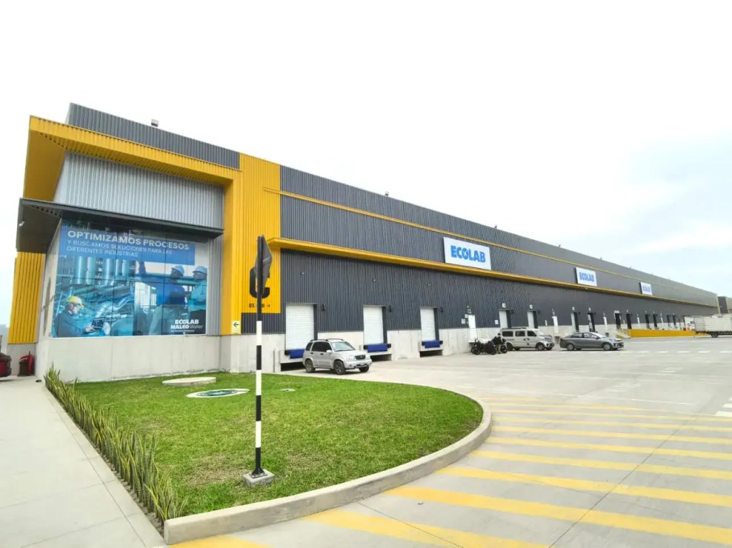 Fachada de la nueva planta de Ecolab en Lurín, Perú, con un diseño moderno y eficiente, rodeada de un área de estacionamiento y paisajismo.