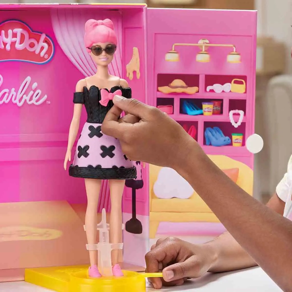 Un niño o niña diseña una vestimenta para una muñeca Barbie con masa moldeable Play-Doh, mostrando un ambiente de juego creativo.
