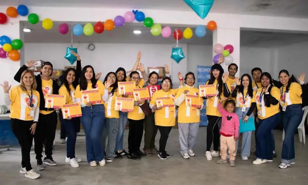 Grupo de voluntarios sonrientes con camisetas amarillas, sosteniendo certificados y sonriendo en un ambiente festivo decorado con globos de colores.