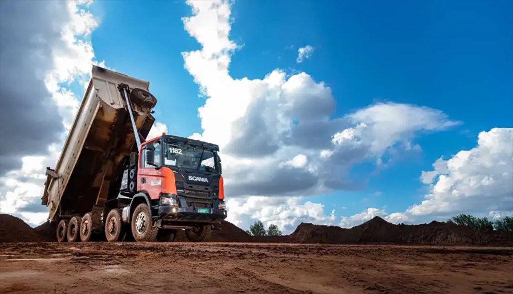 Camión volquete Scania cargando material en un entorno minero bajo un cielo despejado con nubes.