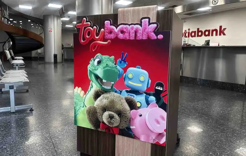 Cartel de la iniciativa 'Toy Bank' de Scotiabank, exhibiendo un dragón de peluche, un robot, un cerdito y un oso de peluche en un ambiente de banco.
