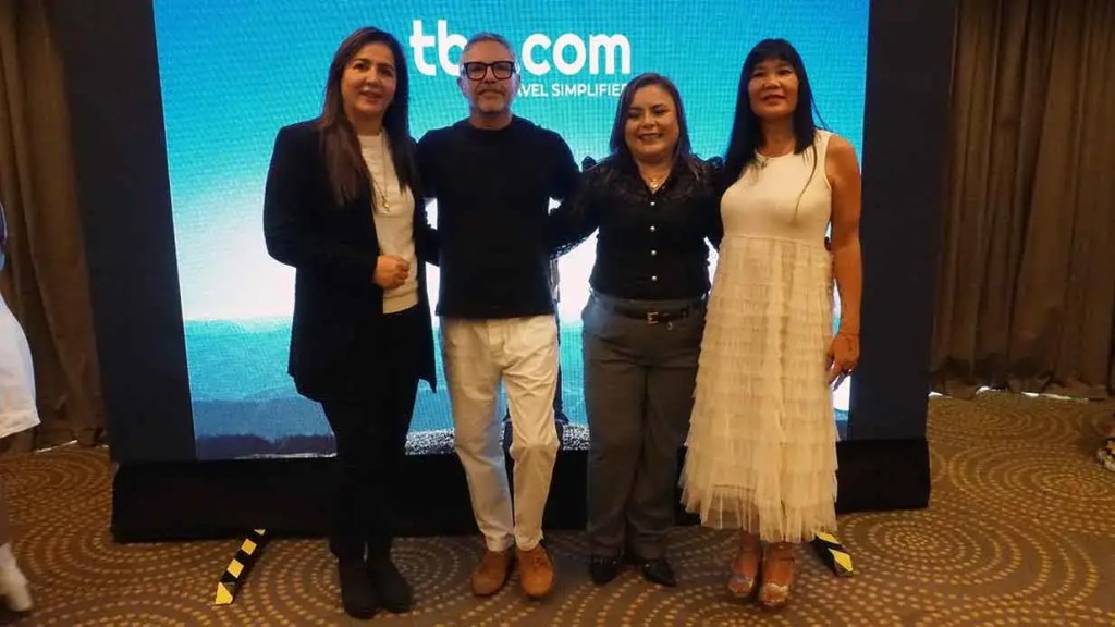 Cuatro personas posando frente a una pantalla con el logo de TBO.COM en un evento turístico.