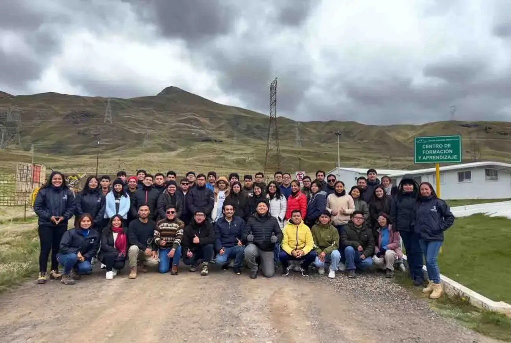 Grupo de jóvenes estudiantes en un área exterior con montañas de fondo, participando en un evento relacionado con el Programa de Prácticas Profesionales de Volcan Compañía Minera.