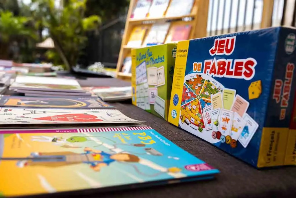 Variety of children's books and educational games displayed on a table outdoors.