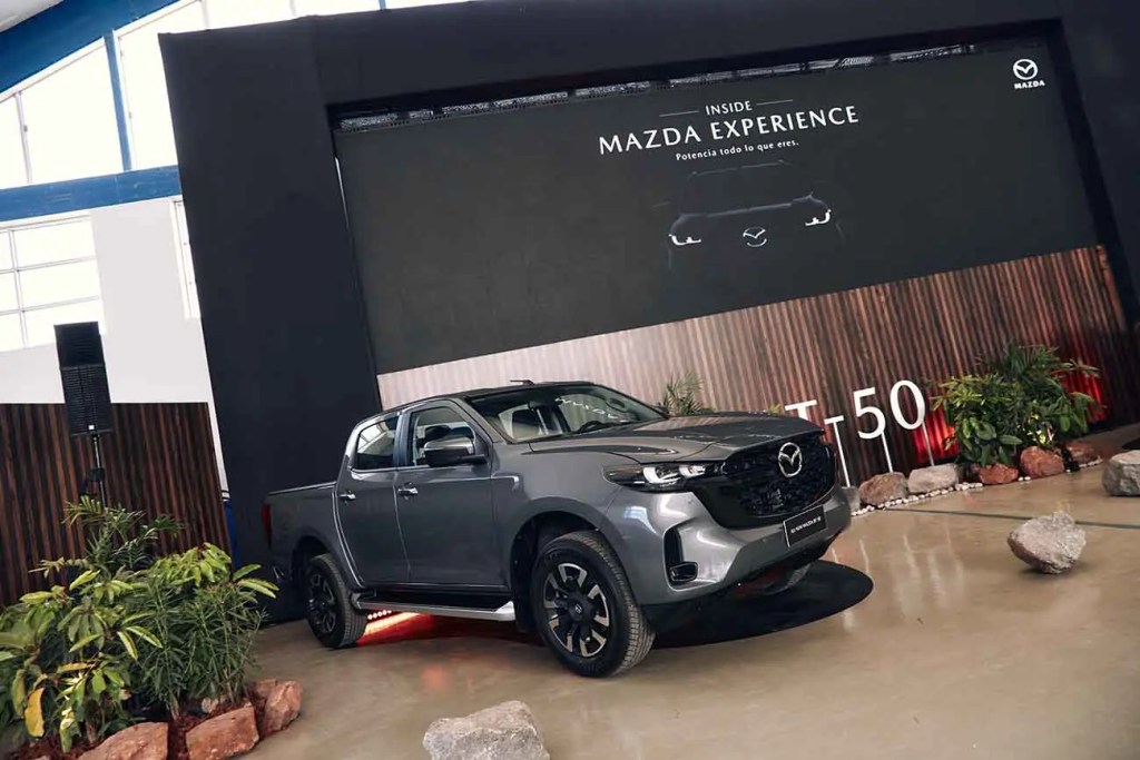 Mazda All New BT-50 pick-up truck displayed in a modern showroom with a large promotional backdrop highlighting its features.