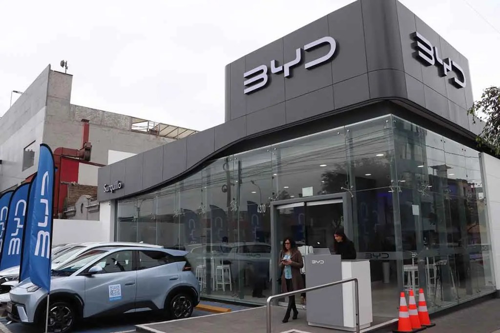 Exterior de la nueva BYD Store Surquillo en Lima, mostrando la fachada moderna, vehículos eléctricos en la exhibición y dos personas en la entrada.
