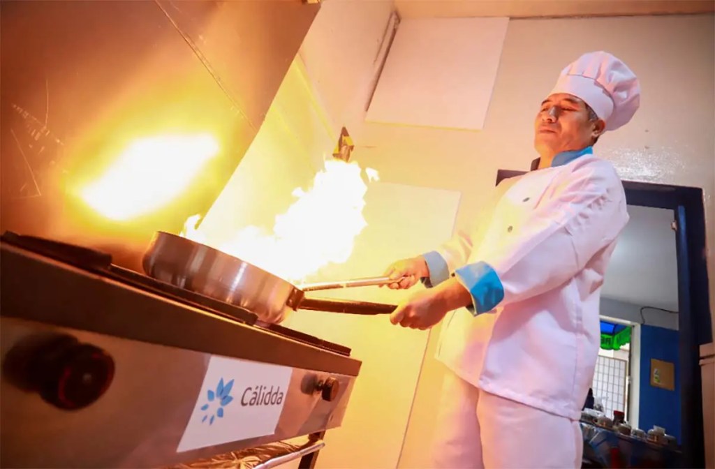 Chef cooking with gas stove, flames rising from a pan, showcasing the use of natural gas in a kitchen.